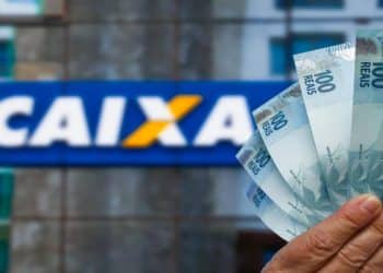 Notas de cem reais em frente à fachada da Caixa, banco que paga o Abono Salarial e o ressarcimento do PIS/Pasep.