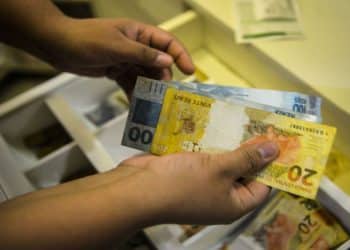 Mãos segurando notas de 20 e 100 reais próximas a caixa registradora aberta, simbolizando o pagamento de R$ 4.521,00.