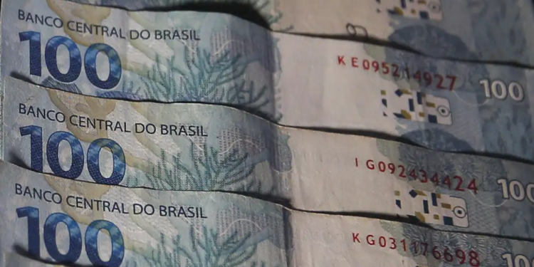 Notas de 100 reais alinhadas, detalhes do Banco Central visíveis, fundo escuro, simbolizando o pagamento do valor de R$ 8.475,55 do INSS.