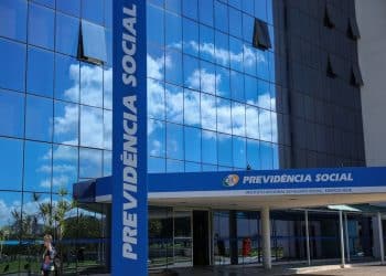 Fachada espelhada do prédio do INSS com letreiros Previdência Social e mulher caminhando, simbolizando o pagamento do valor de R$ 8.475,55, atual teto do INSS.