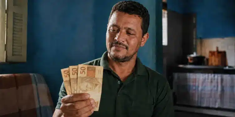 Trabalhador brasileiro segurando notas de R$ 50 com expressão de expectativa, representando a liberação de R$811 para quem trabalhou 6 meses em 2024.