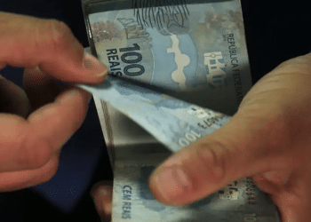 Mãos contam maço de cédulas de cem reais em close