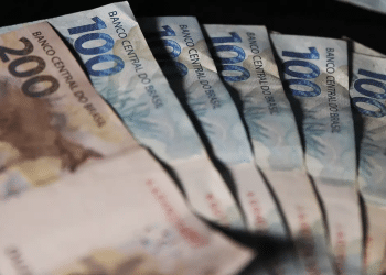 Cédulas de real de cem e duzentos reais dispostas em leque sobre fundo escuro, simbolizando o pagamento de junho sem o adicional de R$ 810,50.