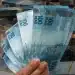 Pessoa segurando cédulas de reais, representando o pagamento de R$ 1.486 para trabalhadores e desempregados com CPF de final 0 a 9.