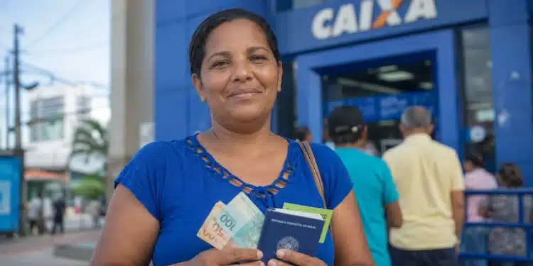 Mulher segura cédulas de reais e documentos em frente a uma agência da Caixa, representando o pagamento unificado do Bolsa Família em junho.