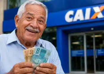 Beneficiário do INSS segura cédulas de real em frente a uma agência da Caixa, representando os pagamentos de junho.