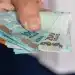 Mão segurando cédulas de real, representando pagamentos do INSS, abono PIS/Pasep e ressarcimentos liberados antes de julho.