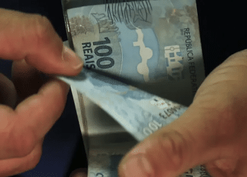 Pessoa conta notas de R$ 100 ao receber os pagamentos liberados para desempregados em 2026