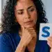 Mulher observando um cartão com a letra “S” enquanto reflete sobre uma regra de português, representando uma palavra em que o plural aparece no meio.