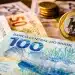 Notas de dinheiro em reais representando a liberação de pagamento do programa Pé-de-Meia em 1º de julho, com foco em benefício educacional.