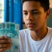 Estudante do ensino médio segurando notas de R$ 100, mostrando o pagamento do programa Pé-de-Meia de junho de R$ 1.000.