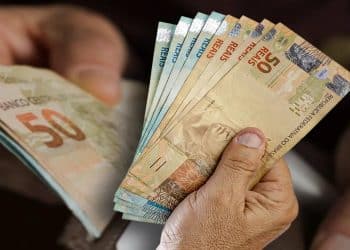 Mãos seguram notas de real representando a restituição de até R$ 1.000 paga via Pix pela Receita Federal