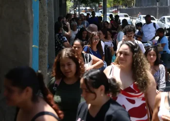 Fila de pessoas caminhando em ambiente urbano durante realização da Prova Nacional Docente.