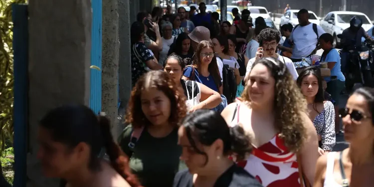 Fila de pessoas caminhando em ambiente urbano durante realização da Prova Nacional Docente.