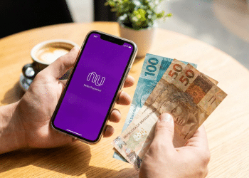 Alt text: Pessoa segurando celular com aplicativo do Nubank e notas de R$ 100 e R$ 50.