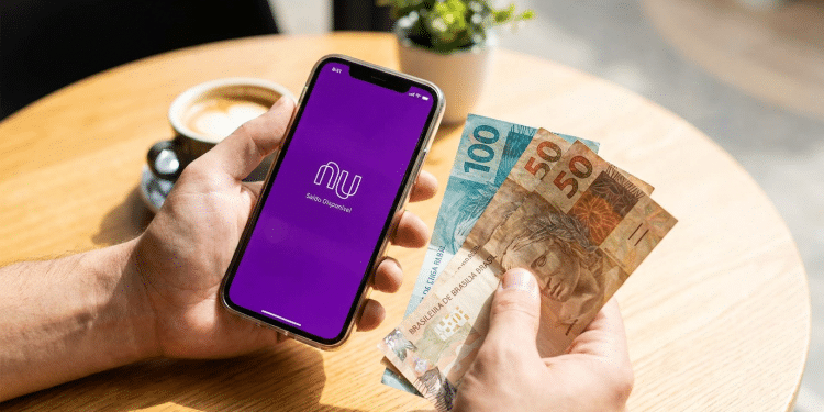 Alt text: Pessoa segurando celular com aplicativo do Nubank e notas de R$ 100 e R$ 50.