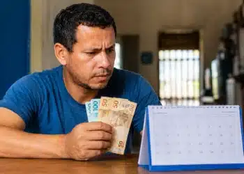 Trabalhador segura cédulas de real enquanto observa calendário para prazo de saque do PIS/Pasep 2026