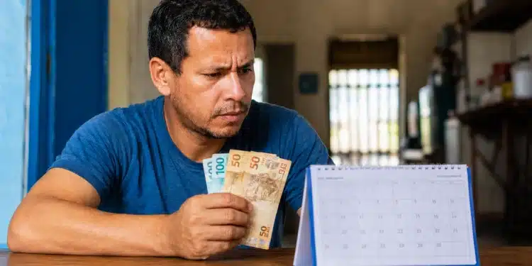 Trabalhador segura cédulas de real enquanto observa calendário para prazo de saque do PIS/Pasep 2026
