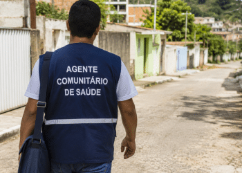 Agente Comunitário de Saúde caminha por rua residencial em imagem sobre vaga aberta na Prefeitura.