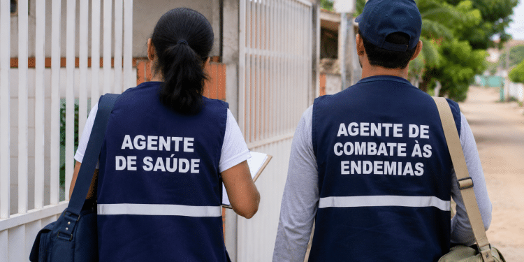 Agente de saúde e agente de combate às endemias fardados de costas durante atendimento em área residencial.