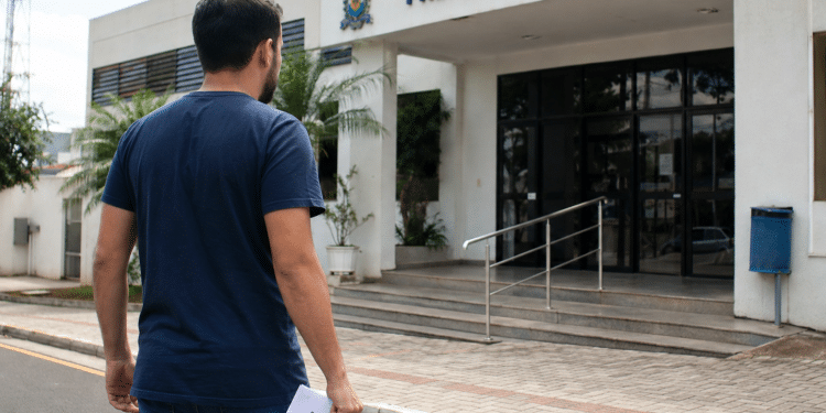 Candidato com documento de processo seletivo em frente à Prefeitura Municipal.