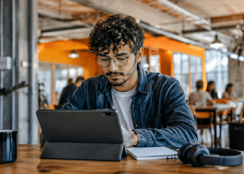 Jovem usando tablet em coworking moderno, representando preparação para profissões do futuro e novas tendências do mercado de trabalho.