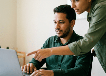 Pessoa em cadeira de rodas recebe orientação sobre inclusão digital em frente ao notebook.
