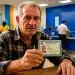Idoso mostrando carteira de identidade em agência bancária, destacando a importância da prova de vida para aposentados em junho.