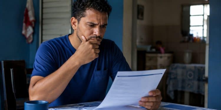 Trabalhador preocupado analisando um documento em casa, representando a conferência das regras e do prazo do seguro-desemprego