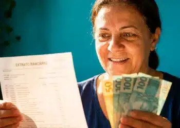 Mulher segura extrato bancário e notas de real após verificar ressarcimento de descontos indevidos do INSS.