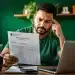 Homem analisando um documento do Imposto de Renda com expressão de preocupação, representando um possível erro nos dados bancários da restituição.