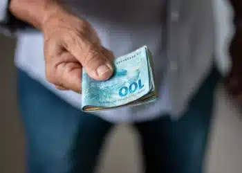 Mão segurando cédulas de dinheiro em real representando situação de conversa sobre salário e limites pessoais.