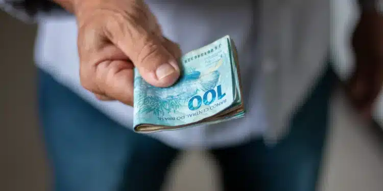 Mão segurando cédulas de dinheiro em real representando situação de conversa sobre salário e limites pessoais.
