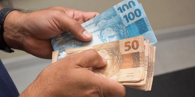 Mãos segurando e contando notas de dinheiro representando saque-aniversário do FGTS.