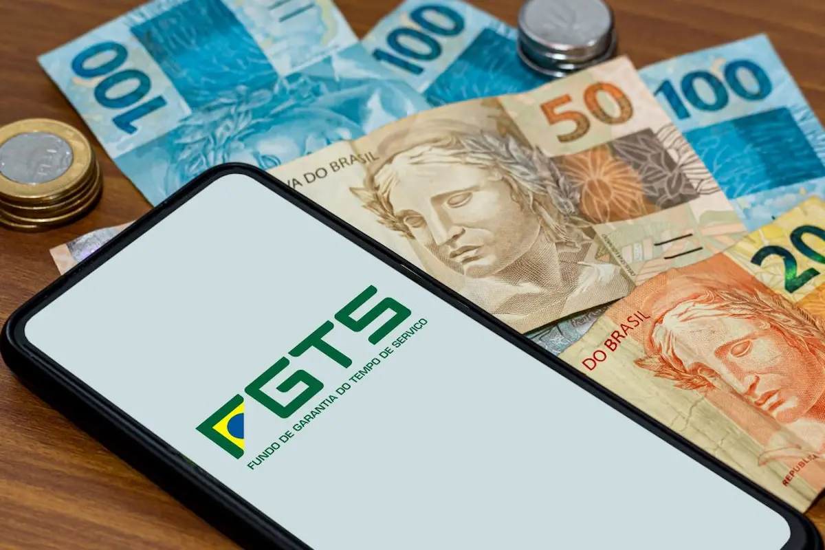 Celular mostrando aplicativo FGTS com cédulas de dinheiro ao redor, representando o saque calamidade.