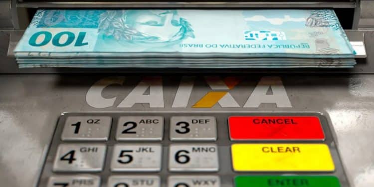 Dinheiro saindo de caixa eletrônico da CAIXA, que paga o Saque Calamidade do FGTS de até R$ 6.220