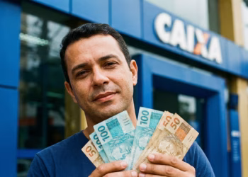 Pessoa em frente a uma agência da Caixa segurando notas de R$ 100 e R$ 50 do Saque Calamidade do FGTS.