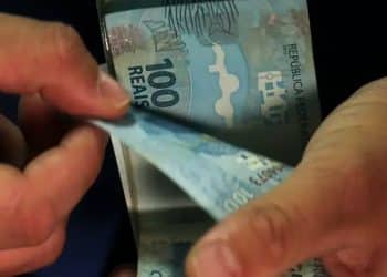 Mãos contando cédulas de R$ 100, representando o saque calamidade do FGTS e as cotas do antigo fundo PIS/Pasep