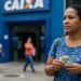 Trabalhadora segura dinheiro em frente a uma agência da Caixa durante prazo do saque calamidade do FGTS.
