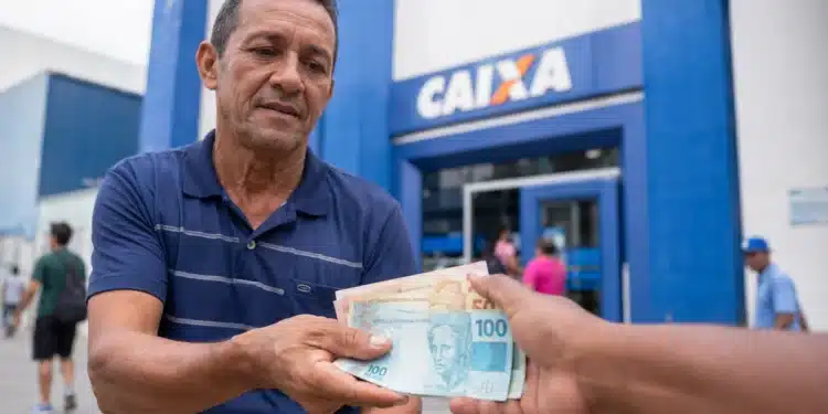 Trabalhador recebendo cédulas de real em frente a uma agência da Caixa, representando o saque de até R$ 1.621 do PIS/Pasep.