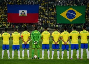 Imagem ilustrativa de jogadores da Seleção Brasileira perfilados em campo diante das bandeiras do Haiti e do Brasil, em referência ao jogo Brasil x Haiti pela Copa do Mundo 2026