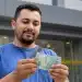 Homem segurando dinheiro em frente a uma agência bancária, ilustrando pagamento da restituição do segundo lote do Imposto de Renda