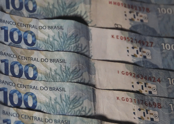 Várias cédulas de 100 reais alinhadas lado a lado, destaque para texturas e cores azuladas, simbolizando o pagamento de R$ 2.518,65, teto do seguro-desemprego 2026.