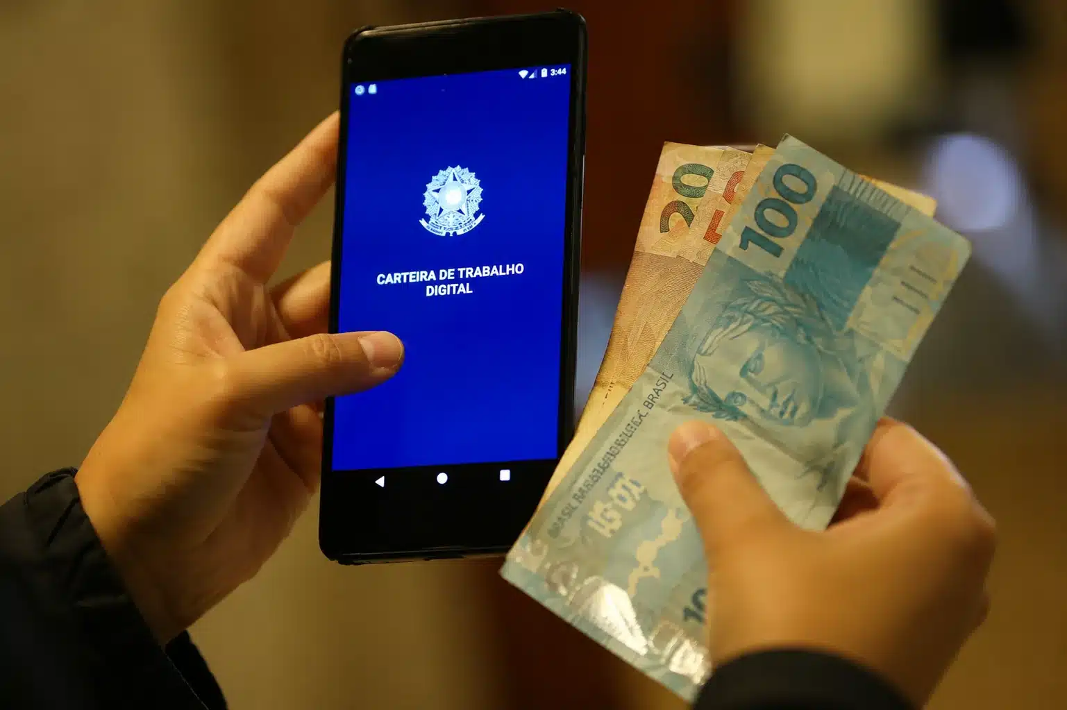 Celular com aplicativo Carteira de Trabalho Digital ao lado de cédulas, representando a solicitação e o acompanhamento do Seguro-Desemprego pelo app