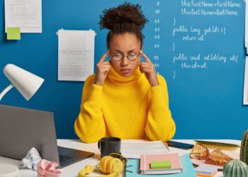 Mulher concentrada leva os dedos às têmporas diante do notebook, tentando se concentrar
