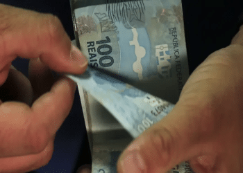 Mãos contando cédulas de R$ 100, ilustrando o teto reajustado do seguro-desemprego em 2026.
