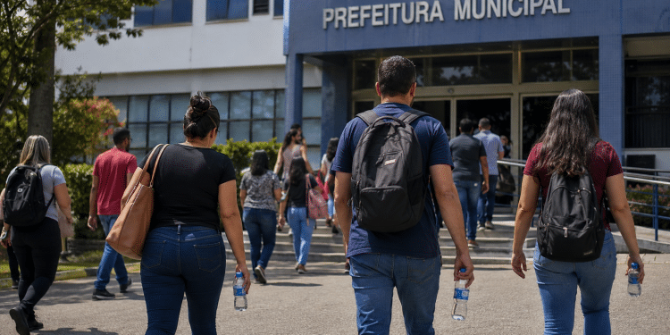 Pessoas caminhando em direção à Prefeitura Municipal com mochilas, bolsas e garrafas de água, representando candidatos de concurso público.