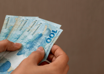 Pessoa contando notas de cem reais com destaque para cédulas brasileiras.