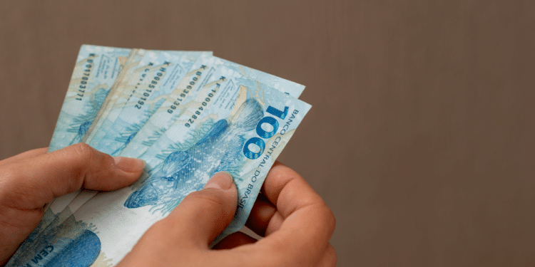 Pessoa contando notas de cem reais com destaque para cédulas brasileiras.