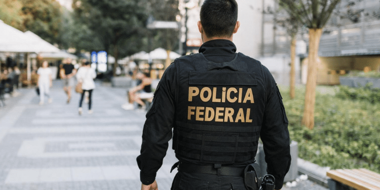 Agente da Polícia Federal patrulha área urbana movimentada.